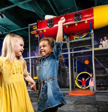 An image of two little girls holding hands and gesturing excitedly while they play at The Strong museum.