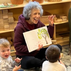 Linda Margolin, sitting in the Woodbury classroom, reading a book to children