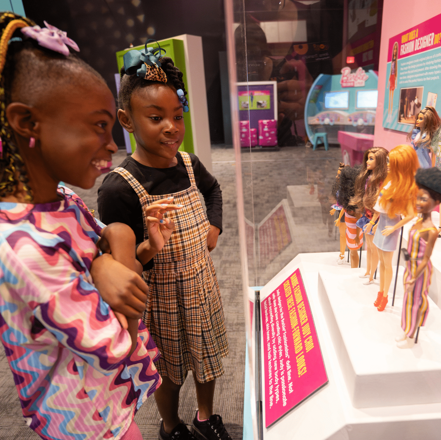 two girls looking at a display case full of barbie dolls