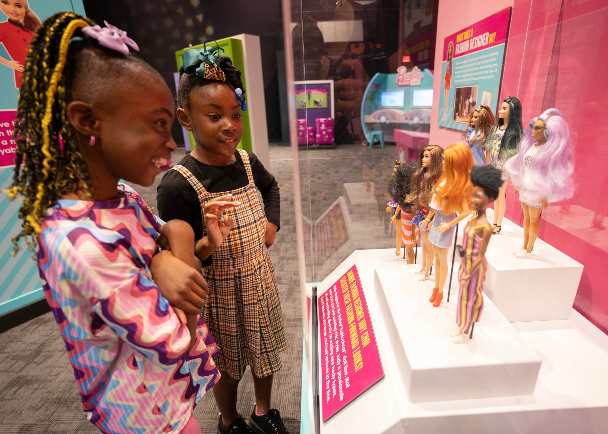 two girls looking at a display case full of barbie dolls