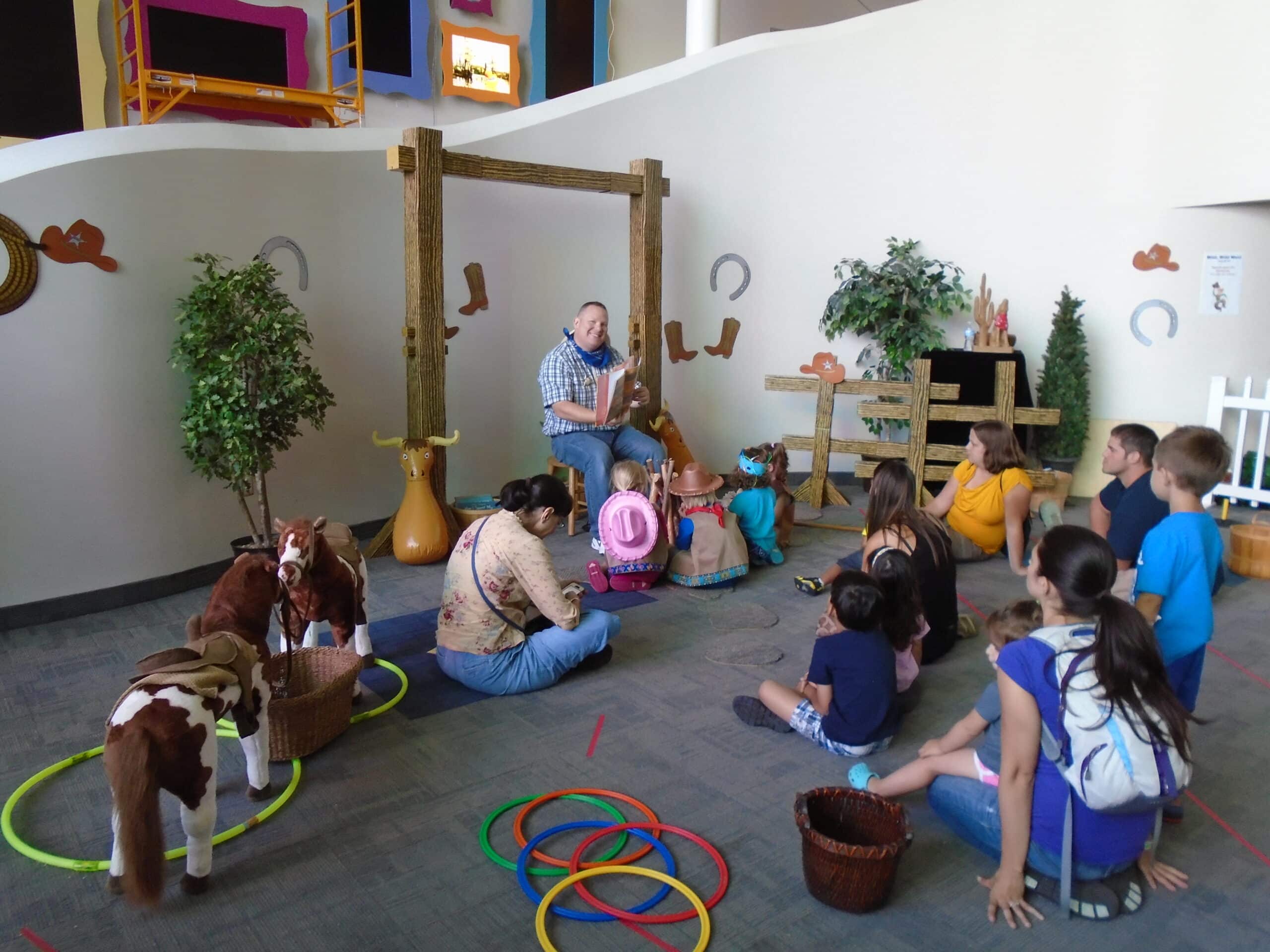 kids wearing rodeo outfits listening to a man dressed as a cowboy tell a story