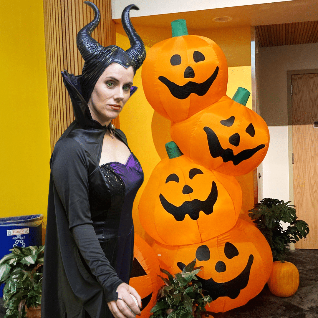 Woman dressed as Maleficent in front of an inflatable stack of Jack-o-lanterns.