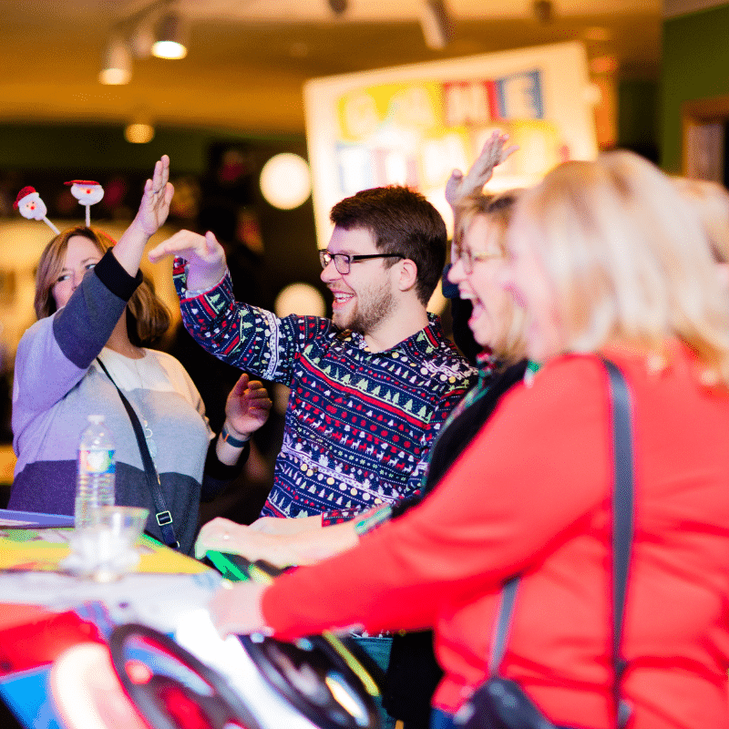 People in Christmas sweaters celebrating a win on an arcade game.