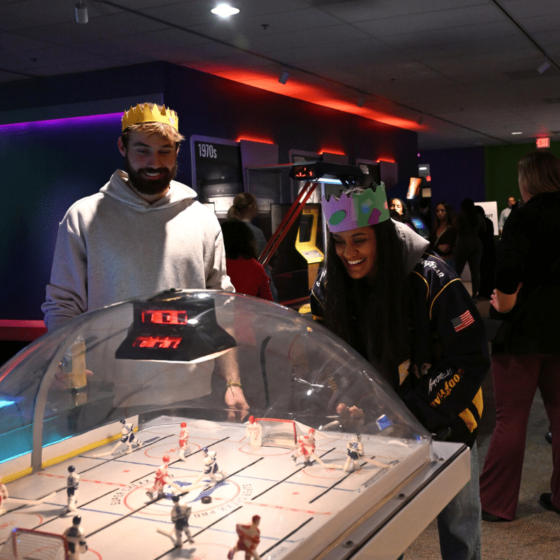 Adults wearing paper crowns play bubble hocky in Infinity Arcade.