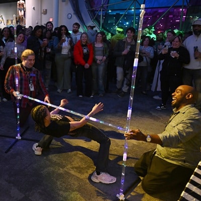 A group of adults circled around a limbo bar with an adult man, mid-limbo attempt.
